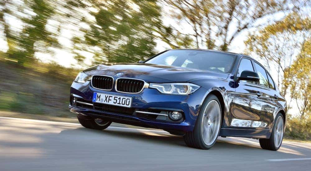 Front angled view of a blue 2015 BMW 3 Series driving down a rural street