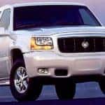 A silver 1999 Cadillac Escalade is shown from the front at an angle after leaving a dealership that advertises used Cadillac for sale.