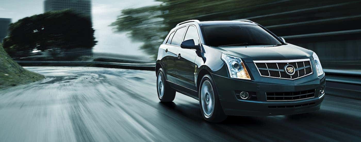 Front view of a black 2012 Cadillac SRX driving on wet pavement near the city