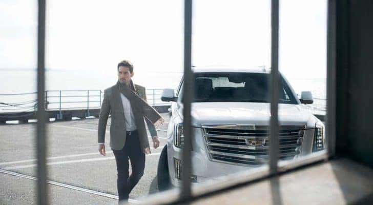 Man walking away from his white 2015 Cadillac Escalade Platinum which is shown through a window
