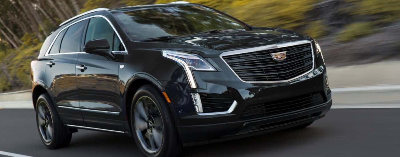 A black 2019 Cadillac XT5 Sport is shown from the side driving on a tree-lined road.