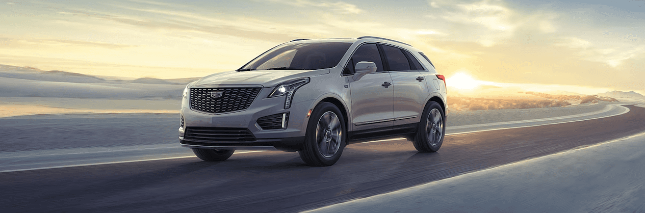 2024 Cadillac XT5 driving on a curved road with the sun setting in the background