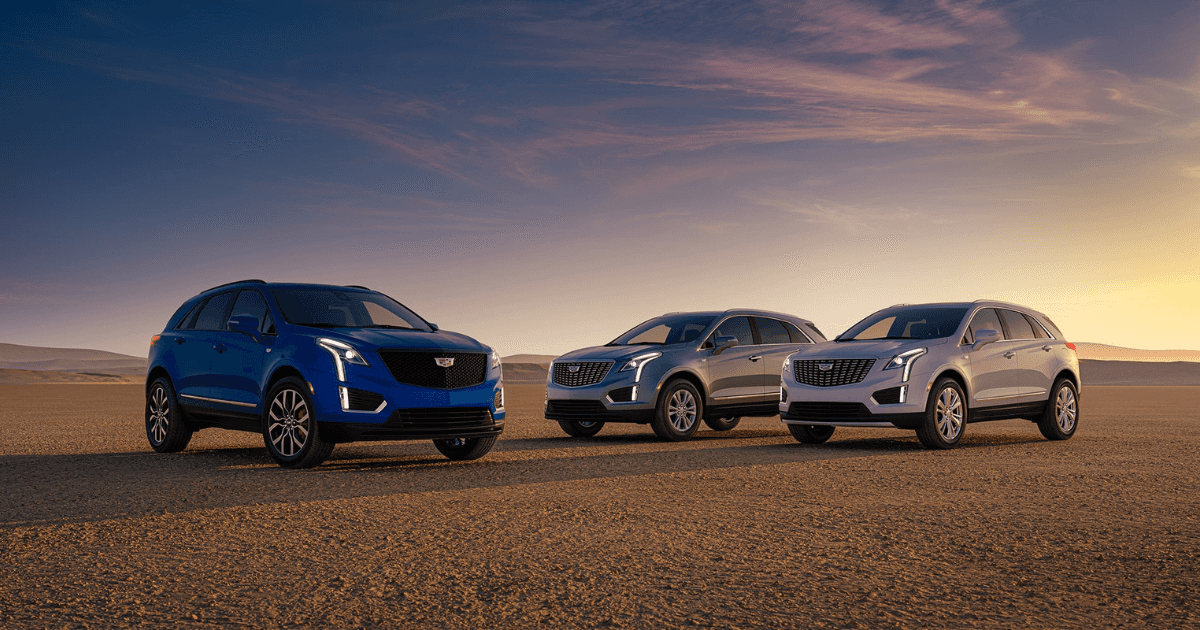 Three Cadillac XT5 models (blue, light gray, and grey) parked on a flat desert during sunset