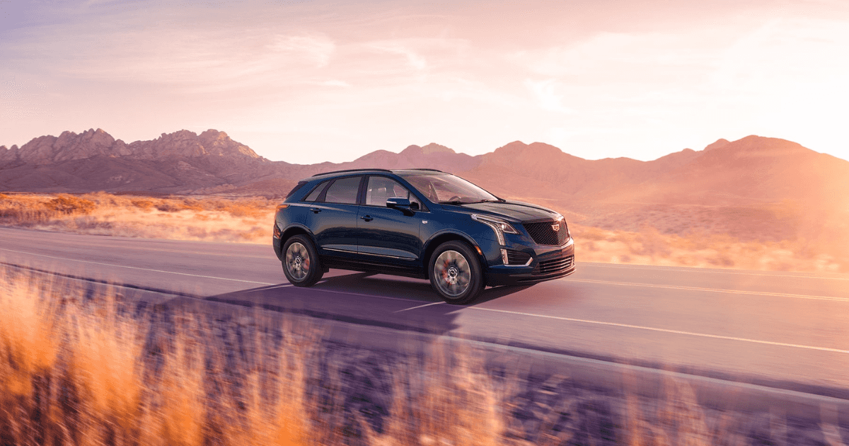 A blue Cadillac XT5 driving down the highway through a desert during sunset