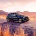 A blue Cadillac XT5 driving down the road through a desert