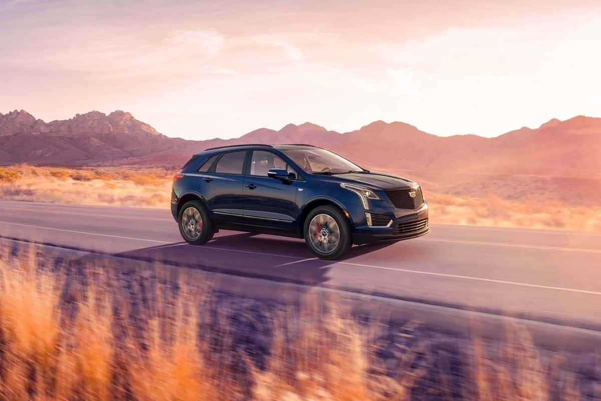 A blue Cadillac XT5 driving down the road through a desert