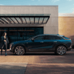 A blue Cadillac LYRIQ in profile, parked in front of a building as a woman walks in front of it