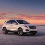A white Cadillac XT5 in a desert while the sun sets.