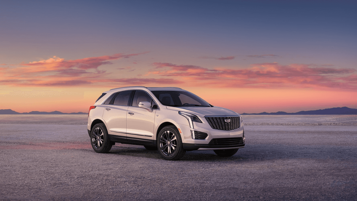 A white Cadillac XT5 in a desert while the sun sets.