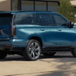 A side view of a blue Cadillac Escalade parked in front of a nice house