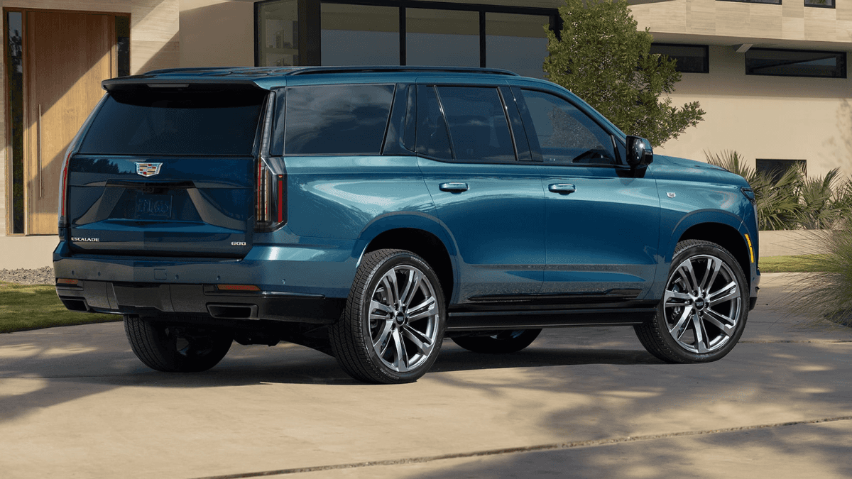 A side view of a blue Cadillac Escalade parked in front of a nice house