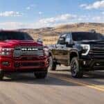 Red 2026 Ram 2500 and black 2026 Chevrolet Silverado 2500 HD driving side by side on a rural road