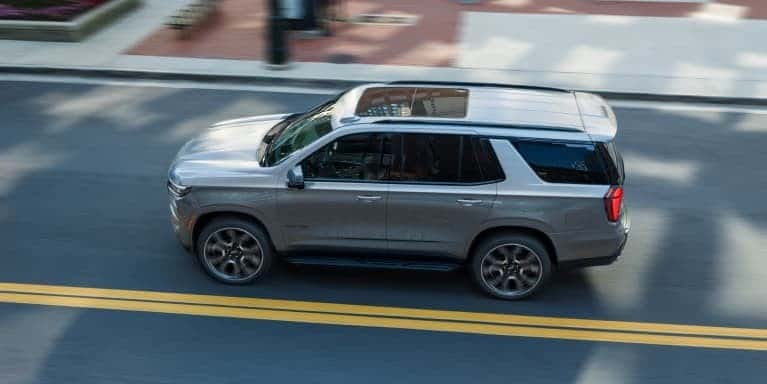 2026 Chevrolet Tahoe driving on a city street in St. George, UT, showcasing its full-size SUV design and capability.