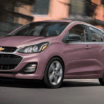 A techno pink Chevy Spark driving in the city