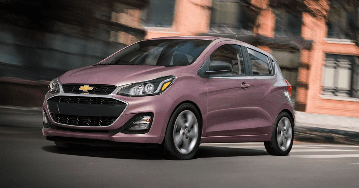 A techno pink Chevy Spark driving in the city
